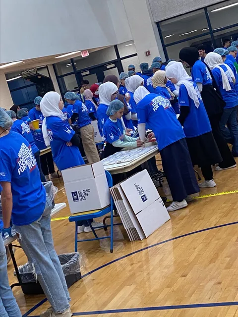 A group of students wearing blue, Islamic Relief package meals in the WVU gymnasium. 