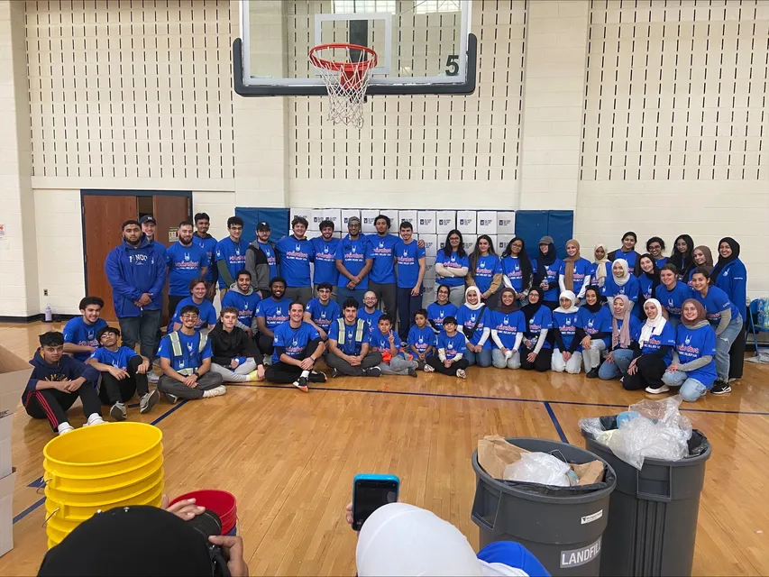 A group of students wearing blue, Islamic Relief shirts pose in a gymnasium. 