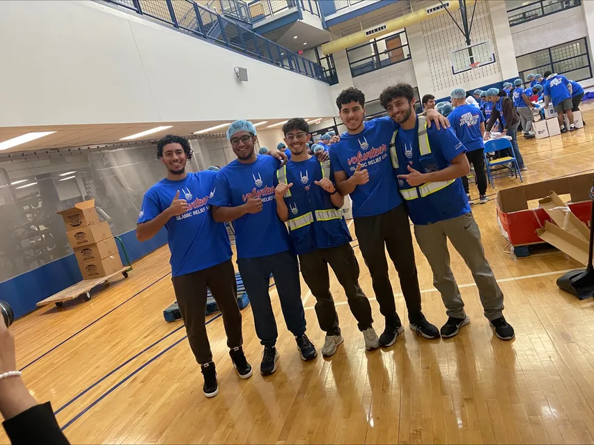 A group of students wearing blue, Islamic Relief shirts pose in a gymnasium. 